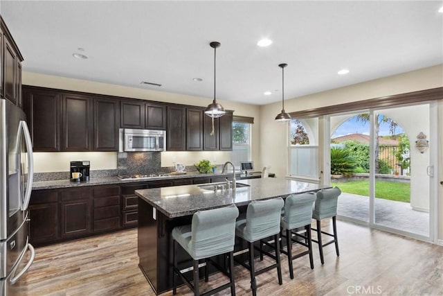 45976 Camino Rubi, Temecula, CA 92592 - kitchen featuring a sink, stainless steel appliances, dark stone counters, light wood-style flooring, and a center island with sink