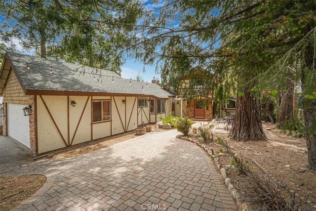 1954 Nob Hill Dr, Running Springs, CA 92382 - back of house featuring stucco siding, a garage, driveway, roof with shingles, and a patio