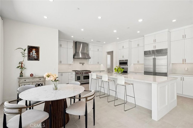 106 Bright Star, Irvine, CA 92618 - kitchen featuring high quality appliances, wall chimney range hood, light countertops, white cabinetry, and a kitchen bar