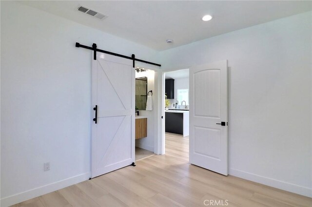2015 W 42nd Pl, Los Angeles, CA 90062 - unfurnished bedroom featuring a barn door, light wood-style flooring, baseboards, and recessed lighting