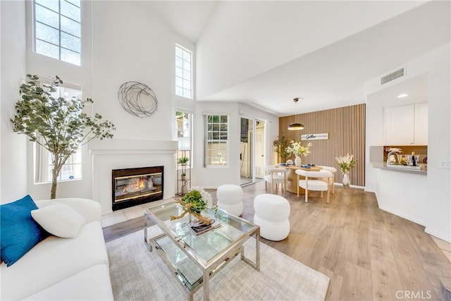 13445 Savanna, Tustin, CA 92782 - living room featuring a towering ceiling, healthy amount of natural light, light wood-style flooring, a glass covered fireplace, and wood walls