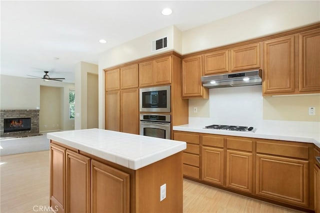 2 Hydrangea St, Ladera Ranch, CA 92694 - kitchen featuring appliances with stainless steel finishes, range hood, tile countertops, a ceiling fan, and a glass covered fireplace