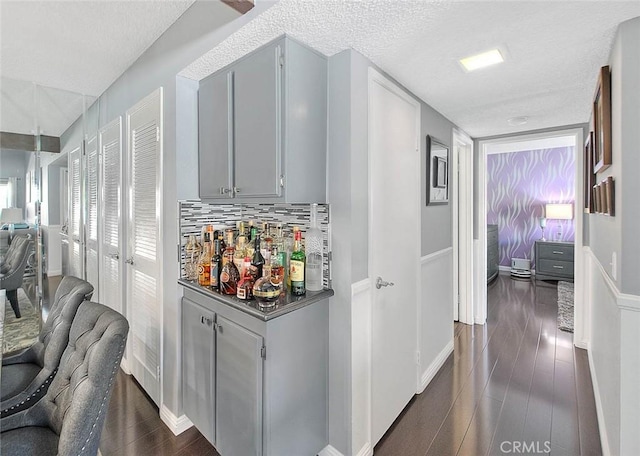 44 Carriage Way Unit 108, Pomona, CA 91766 - bar featuring a textured ceiling, dark wood finished floors, baseboards, and decorative backsplash