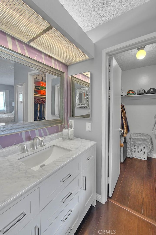 44 Carriage Way Unit 108, Pomona, CA 91766 - bathroom with a textured ceiling, vanity, hardwood / wood-style flooring, baseboards, and a walk in closet