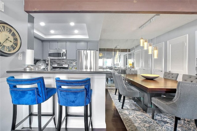 44 Carriage Way Unit 108, Pomona, CA 91766 - kitchen featuring appliances with stainless steel finishes, dark countertops, dark wood-style floors, a raised ceiling, and gray cabinetry