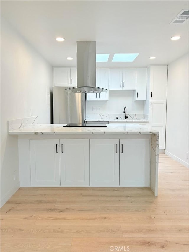 3088 Via Serena N Unit D, Laguna Woods, CA 92637 - kitchen featuring island range hood, white cabinets, a skylight, a sink, and baseboards
