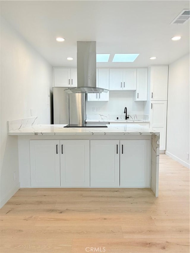 3088 Via Serena N Unit D, Laguna Woods, CA 92637 - kitchen with island range hood, white cabinets, a skylight, light countertops, and baseboards