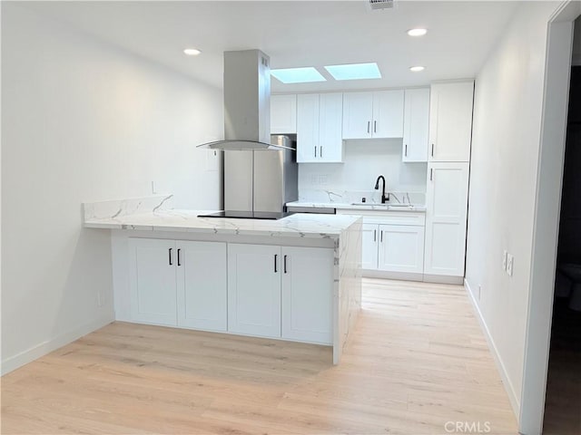 3088 Via Serena N Unit D, Laguna Woods, CA 92637 - kitchen with island range hood, a sink, a skylight, a peninsula, and white cabinetry