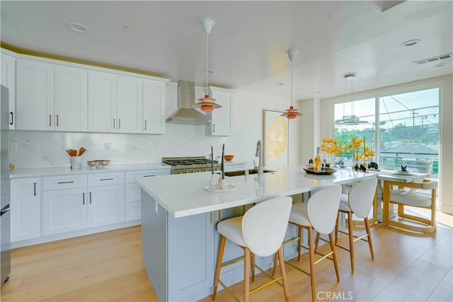 712 N Chestnut Ave, Los Angeles, CA 90042 - kitchen featuring wall chimney range hood, light countertops, an island with sink, tasteful backsplash, and light wood-style flooring