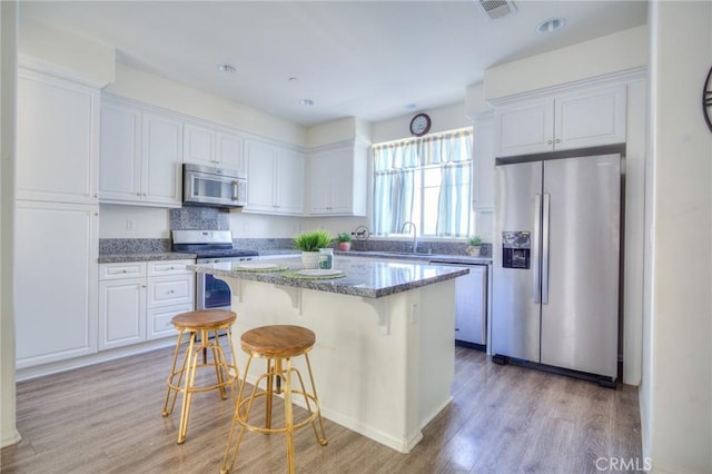 12456 Cassiopeia Ct, Eastvale, CA 91752 - kitchen with appliances with stainless steel finishes, white cabinetry, light wood-style floors, a breakfast bar, and a center island