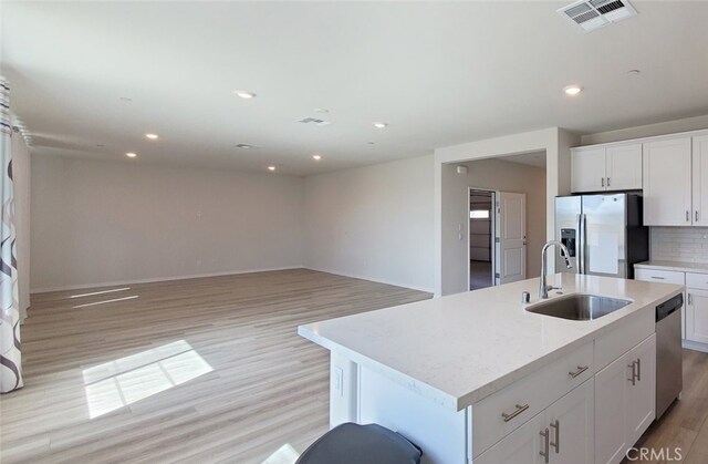 24311 Insignia Dr, Menifee, CA 92584 - kitchen with a sink, stainless steel appliances, light wood-style floors, tasteful backsplash, and a kitchen island with sink