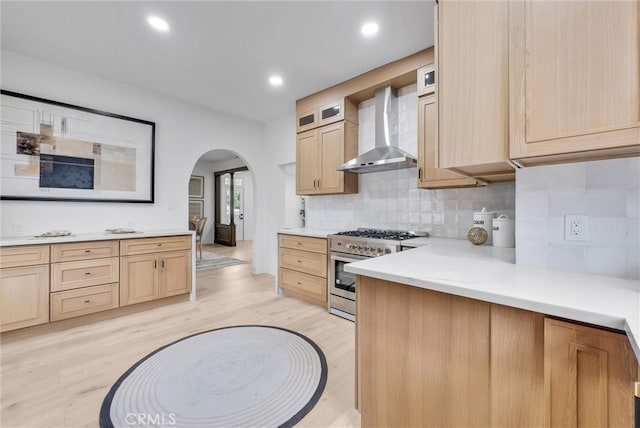 239 N San Antonio Ave, Upland, CA 91786 - kitchen featuring wall chimney range hood, high end range, light brown cabinets, arched walkways, and light wood-style flooring