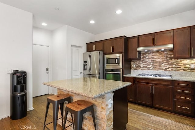 29463 Bouris Dr, Menifee, CA 92584 - kitchen with stainless steel appliances, a kitchen breakfast bar, under cabinet range hood, light wood-style floors, and backsplash