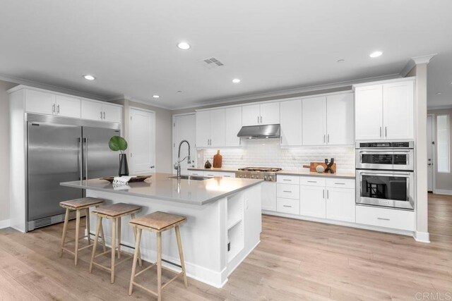 13403 Hudson Ln, San Diego, CA 92130 - kitchen featuring stainless steel appliances, under cabinet range hood, crown molding, decorative backsplash, and white cabinetry