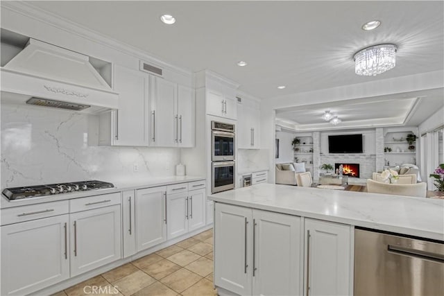 18238 Hastings Way, Porter Ranch, CA 91326 - kitchen featuring premium range hood, appliances with stainless steel finishes, white cabinets, tasteful backsplash, and a warm lit fireplace