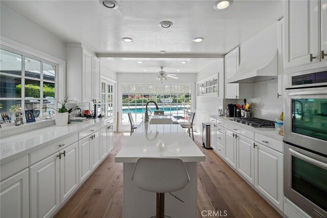 4420 Conchita Way, Tarzana, CA 91356 - kitchen featuring stainless steel appliances, white cabinets, light countertops, a center island with sink, and wood finished floors