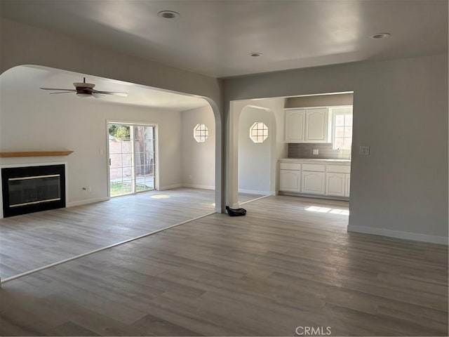 516 W 228th St, Carson, CA 90745 - unfurnished living room with arched walkways, a ceiling fan, light wood-type flooring, baseboards, and a glass covered fireplace