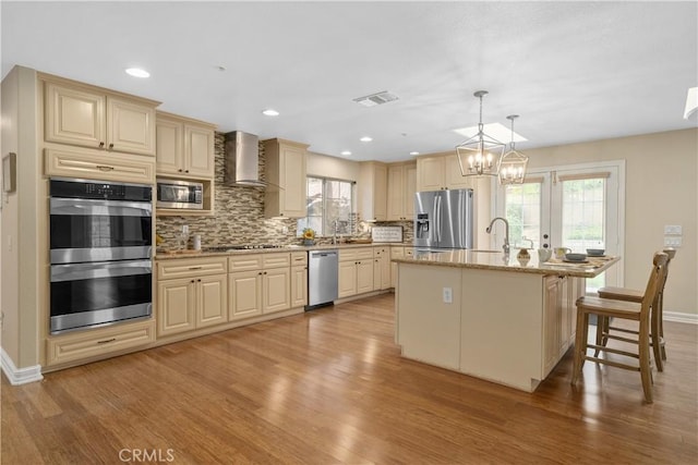 1641 Ford St, Redlands, CA 92373 - kitchen with wall chimney range hood, stainless steel appliances, light wood-type flooring, backsplash, and a chandelier