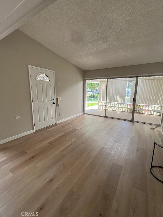 13962 El Dorado Dr Unit M2-60E, Seal Beach, CA 90740 - unfurnished living room featuring light wood finished floors, baseboards, a textured ceiling, and lofted ceiling