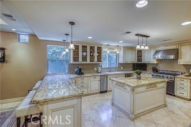 19162 Liggett St, Northridge, CA 91324 - kitchen with high end stainless steel range, under cabinet range hood, backsplash, glass insert cabinets, and light stone countertops