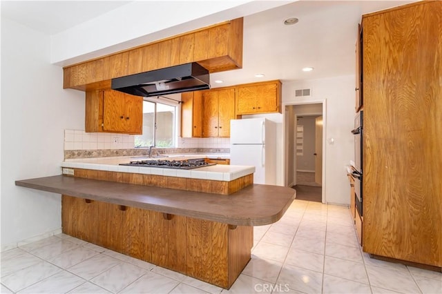 15903 Bryant St, North Hills, CA 91343 - kitchen with freestanding refrigerator, a peninsula, under cabinet range hood, stainless steel gas stovetop, and brown cabinets
