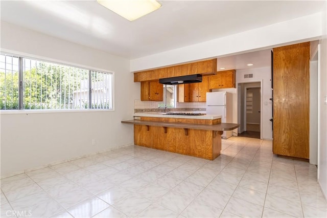 15903 Bryant St, North Hills, CA 91343 - kitchen featuring brown cabinetry, freestanding refrigerator, a peninsula, backsplash, and a breakfast bar