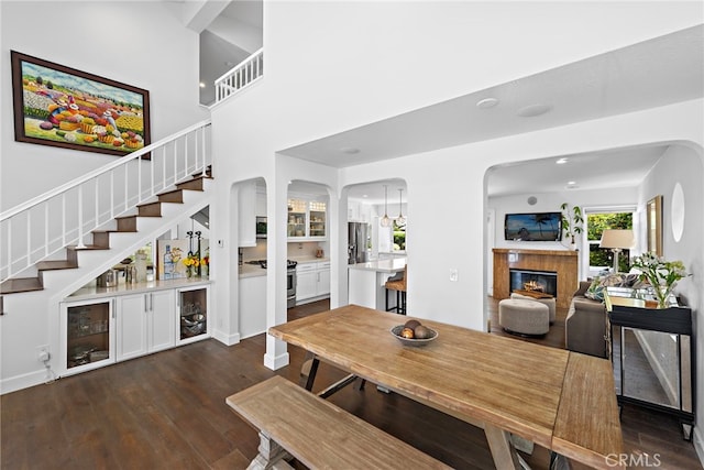 24532 Kings, Laguna Niguel, CA 92677 - dining space with stairway, a glass covered fireplace, arched walkways, dark wood-type flooring, and a high ceiling