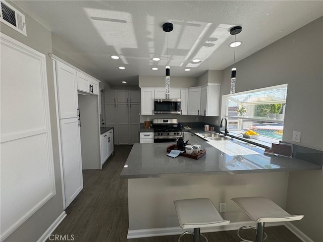 38422 Puma Ln, Palmdale, CA 93551 - kitchen with appliances with stainless steel finishes, a sink, dark wood-style flooring, white cabinetry, and a peninsula