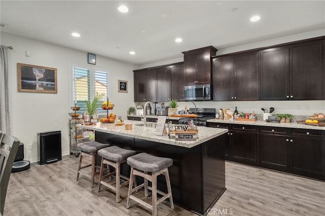 14226 Bonavento Ln, Beaumont, CA 92223 - kitchen with appliances with stainless steel finishes, a kitchen breakfast bar, light stone countertops, light wood-style floors, and an island with sink