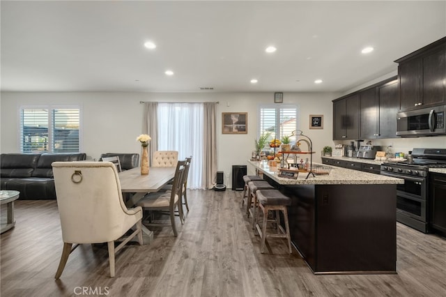 14226 Bonavento Ln, Beaumont, CA 92223 - kitchen with appliances with stainless steel finishes, a kitchen island with sink, wood finished floors, recessed lighting, and plenty of natural light
