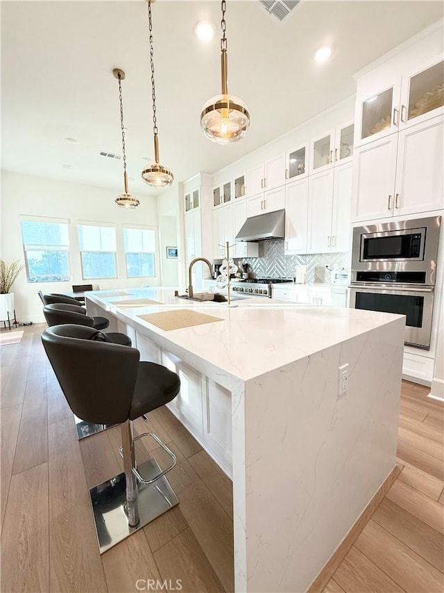 8896 Los Coyotes Ct Unit 410, Buena Park, CA 90621 - kitchen featuring under cabinet range hood, stainless steel appliances, an island with sink, backsplash, and white cabinets