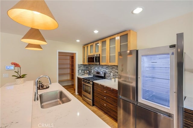 5112 Topanga Canyon Blvd, Woodland Hills, CA 91364 - kitchen with appliances with stainless steel finishes, a sink, light wood finished floors, decorative backsplash, and glass insert cabinets