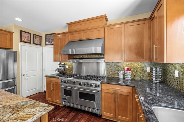 4267 Carnegie Ct, Riverside, CA 92505 - kitchen featuring wall chimney range hood, stainless steel appliances, dark wood-style floors, dark stone countertops, and decorative backsplash