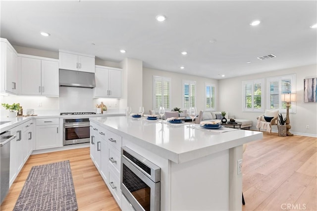 25 Splendor Way, Rancho Mission Viejo, CA 92694 - kitchen with appliances with stainless steel finishes, under cabinet range hood, open floor plan, a kitchen island, and light wood-style flooring