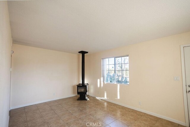 58382 Sunny Sands Dr, Yucca Valley, CA 92284 - empty room featuring a wood stove, a textured ceiling, light tile patterned flooring, and baseboards