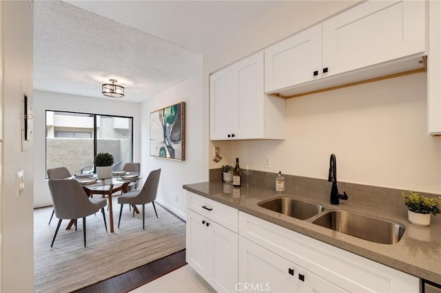 849 E Victoria St Unit 210, Carson, CA 90746 - kitchen featuring a sink, white cabinetry, baseboards, a textured ceiling, and dark stone countertops
