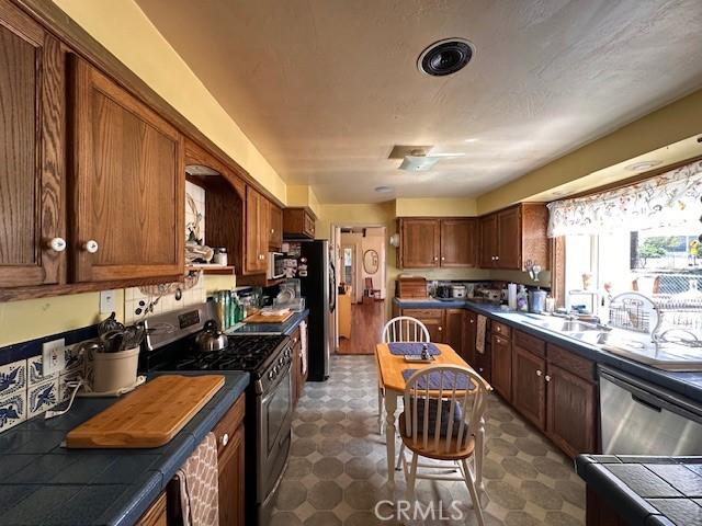 2968 Mill Creek Rd, Mentone, CA 92359 - kitchen with appliances with stainless steel finishes, dark flooring, dark countertops, and brown cabinetry
