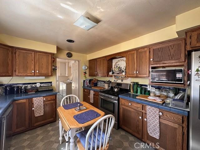 2968 Mill Creek Rd, Mentone, CA 92359 - kitchen with appliances with stainless steel finishes, dark floors, dark countertops, and brown cabinets
