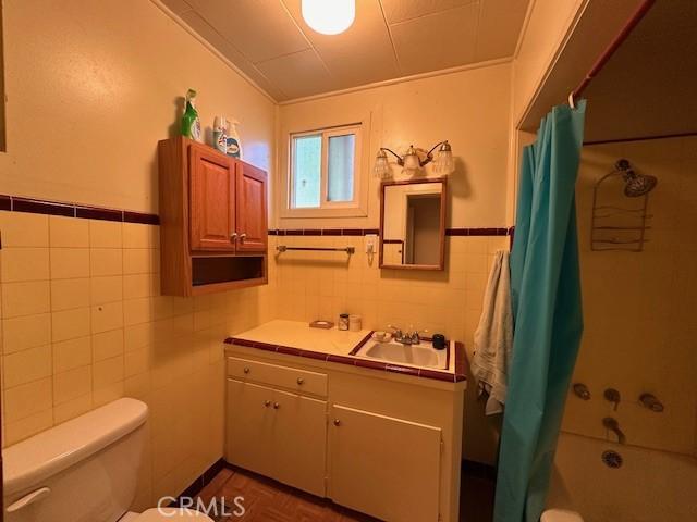 2968 Mill Creek Rd, Mentone, CA 92359 - full bath featuring tile walls, vanity, toilet, wainscoting, and shower / tub combo with curtain