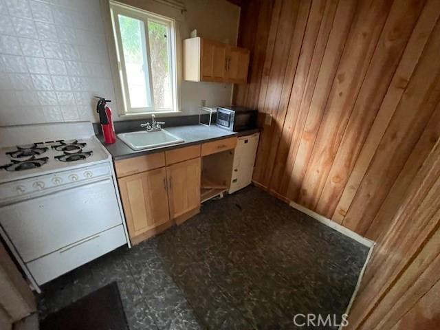 2968 Mill Creek Rd, Mentone, CA 92359 - kitchen featuring white range with gas cooktop, a sink, wooden walls, dark floors, and stainless steel microwave