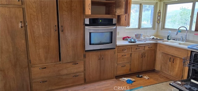 56994 Crestview Dr, Yucca Valley, CA 92284 - kitchen with stainless steel oven, light countertops, light wood-style flooring, brown cabinetry, and backsplash