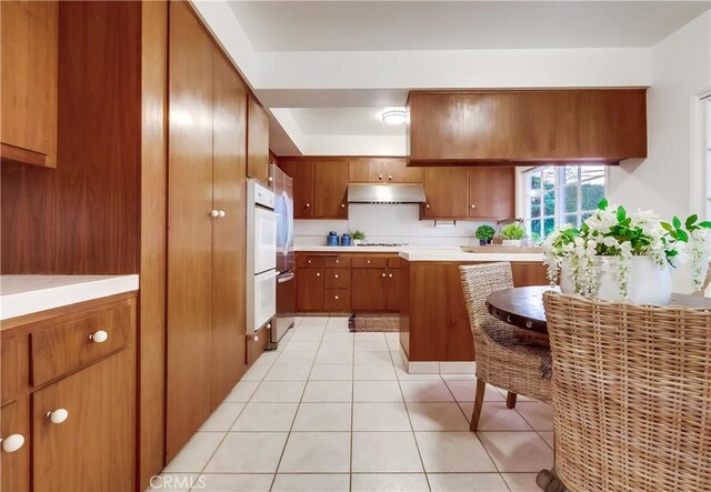 6604 Via Siena, Rancho Palos Verdes, CA 90275 - kitchen with under cabinet range hood, brown cabinetry, light tile patterned floors, and light countertops