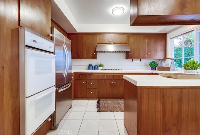 6604 Via Siena, Rancho Palos Verdes, CA 90275 - kitchen featuring under cabinet range hood, white appliances, brown cabinets, light tile patterned floors, and tile counters