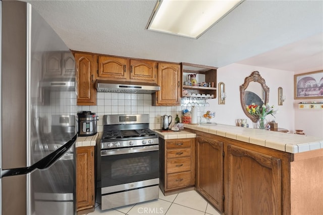 9637 San Carlos Ave, South Gate, CA 90280 - kitchen with appliances with stainless steel finishes, under cabinet range hood, a peninsula, brown cabinetry, and tile countertops