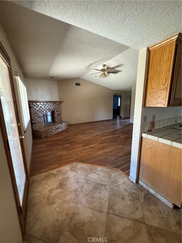 18515 Kalin Ranch Dr, Victorville, CA 92395 - unfurnished living room with vaulted ceiling, wood finished floors, ceiling fan, a fireplace, and a textured ceiling