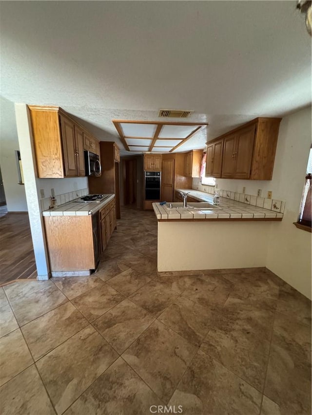 18515 Kalin Ranch Dr, Victorville, CA 92395 - kitchen featuring tile countertops, a peninsula, brown cabinetry, and gas cooktop