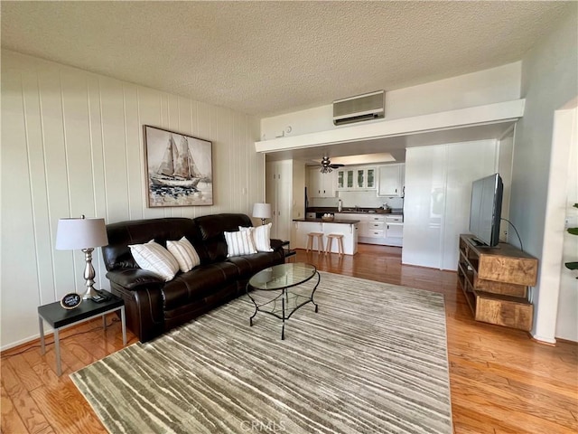 13721 El Dorado Dr Unit M3-K, Seal Beach, CA 90740 - living room featuring light wood-style floors, a ceiling fan, a wall mounted air conditioner, and a textured ceiling