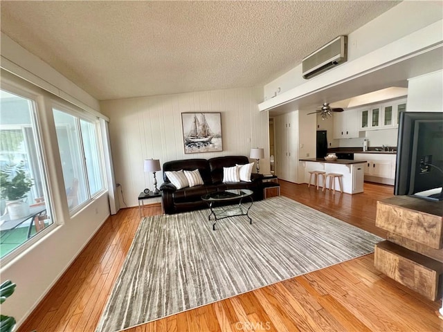 13721 El Dorado Dr Unit M3-K, Seal Beach, CA 90740 - living area with a wall mounted air conditioner, a textured ceiling, light wood-style floors, and a ceiling fan