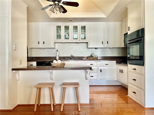 13721 El Dorado Dr Unit M3-K, Seal Beach, CA 90740 - kitchen with black oven, a ceiling fan, white cabinets, a breakfast bar area, and a peninsula