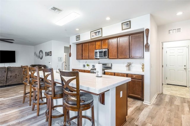 1413 La Quinta Way, Madera, CA 93638 - kitchen with appliances with stainless steel finishes, tile countertops, a breakfast bar area, light wood-style floors, and open floor plan